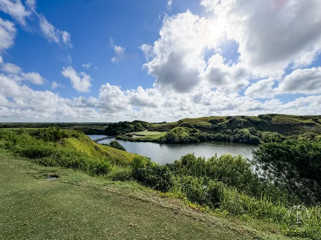 A golfer standing in a sandy waste area at the Blue Course, with a green and the Streamsong lodge in the distance.