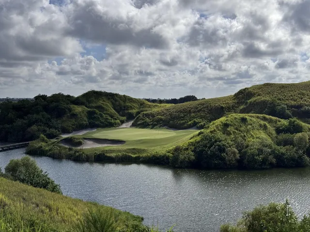 A green and flagstick at the Blue Course, with sand and long grass around the hole and the Streamsong lodge behind it.