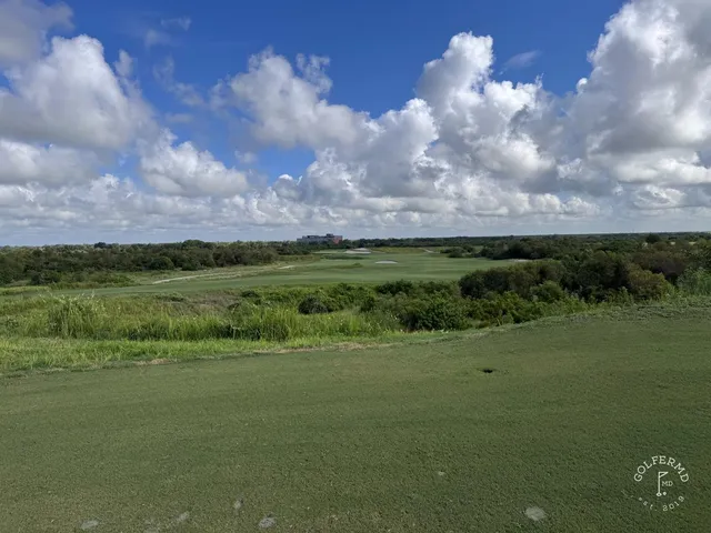 A green and flagstick at the Blue Course, with a sand bunker wrapping the front and dunes behind the hole.