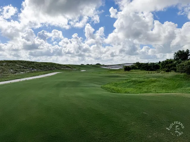 A wide view across the Blue Course, with sand, long grass, and a distant green under a big sky.