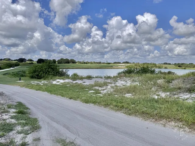 A green and flagstick at the Blue Course, seen across sandy ground, with the Streamsong lodge in the distance.