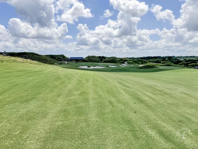 A close view of a green and flagstick at the Blue Course, with sand and the Streamsong lodge behind the hole.