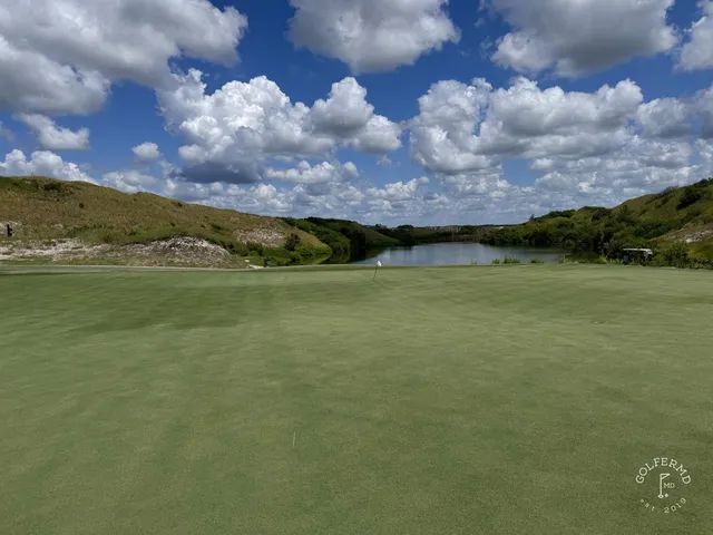 A green and flagstick at the Red Course, with a deep sand bunker beside the green and dunes behind it.