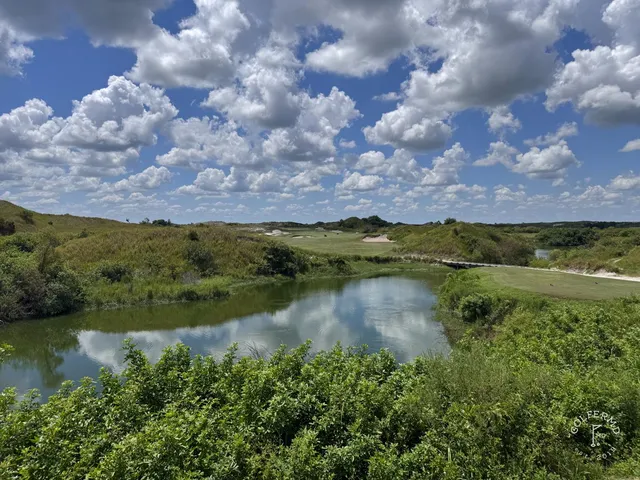 A green and flagstick at the Red Course, seen across sand and long grass, with the Streamsong lodge in the distance.