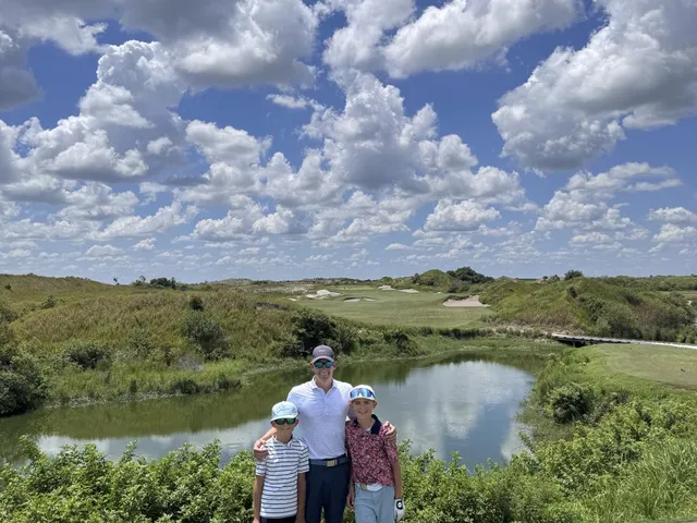 A wide view of the Red Course, with sand waste areas, long grass, and a distant green.