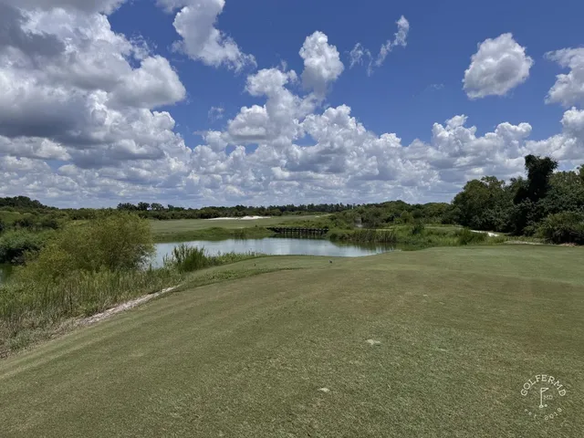 A green and flagstick at the Red Course, with a large sand bunker in the foreground and the Streamsong lodge behind the hole.