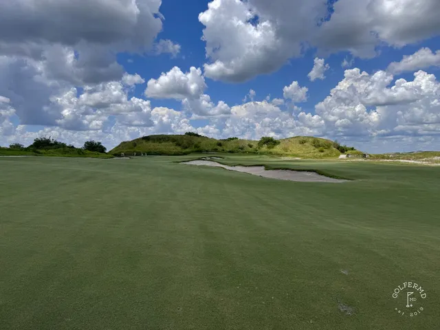 A fairway at the Red Course running between dunes toward a green under a cloudy sky.