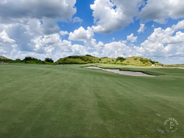 A green and flagstick at the Red Course, with sand and long grass around the hole and the Streamsong lodge behind it.