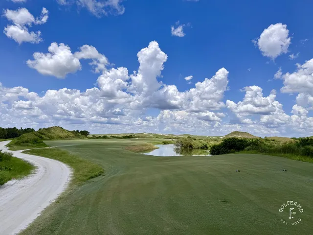 A golfer hitting a shot from a sandy area at the Red Course, with a green and flagstick ahead.