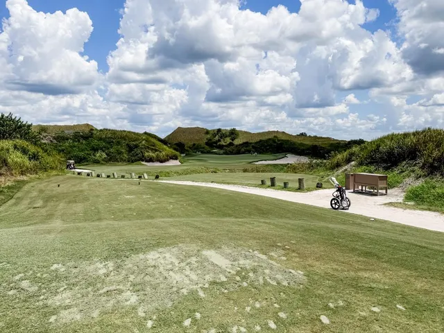 A green and flagstick at the Red Course, seen from a rise, with sand bunkers and the Streamsong lodge in the distance.