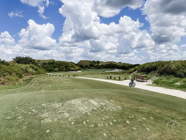 A fairway at the Red Course winding through sand and long grass toward a distant green.