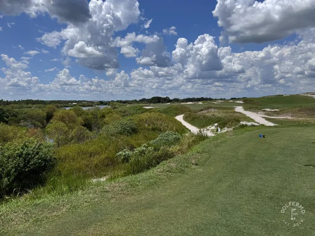 A green and flagstick at the Red Course, with a sand bunker in front and rolling dunes behind the hole.