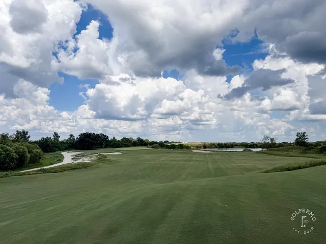 A wide sandy landscape at the Red Course, with a green, long grass, and the Streamsong lodge on the horizon.