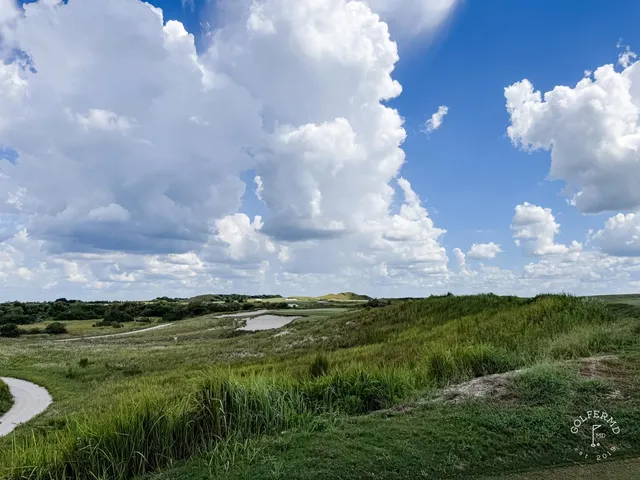 A fairway at the Red Course running through dunes toward a green, with the Streamsong lodge in the distance.