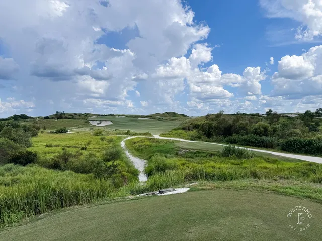 A green and flagstick at the Red Course, with sand and long grass around the hole.