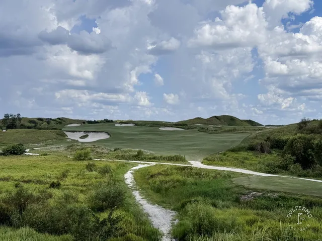 A golfer putting on a green at the Red Course, with sand bunkers and the Streamsong lodge behind the hole.