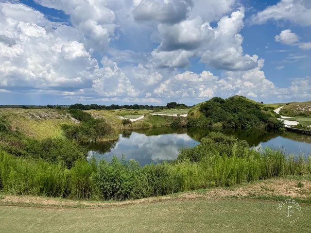 A close view of a green and flagstick at the Red Course, with a sand bunker and the Streamsong lodge behind the hole.
