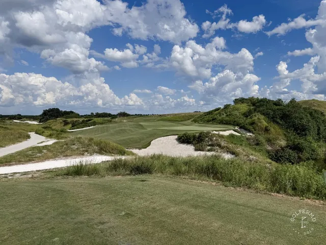 A wide view across the Red Course, with sand, long grass, and a distant green under a big sky.