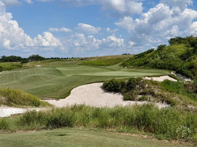 A fairway and green at the Red Course, with sandy ground, long grass, and the Streamsong lodge on the horizon.