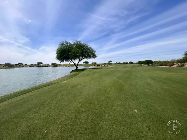 A golfer hitting a shot from a desert waste area at TPC Scottsdale, with the McDowell Mountains behind the hole.