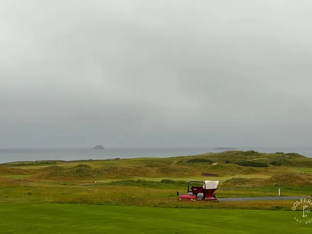A green and flagstick at Tralee, with a bunker in front and the ocean behind the hole.