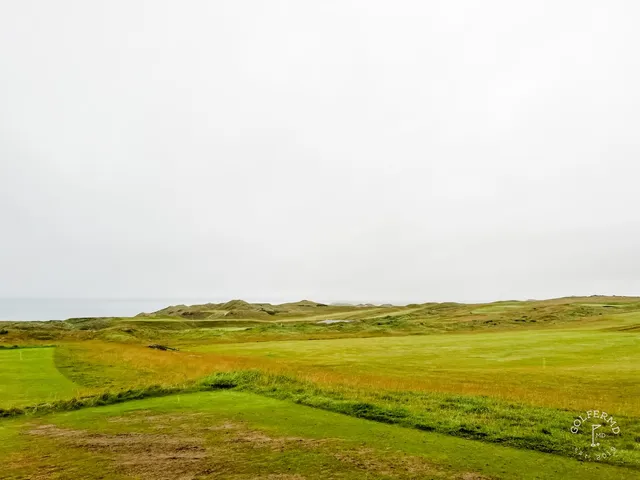 A golfer hitting a shot at Tralee, with the water ahead.