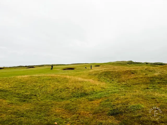 A green and flagstick at Tralee seen from the fairway, with the sea on the horizon.