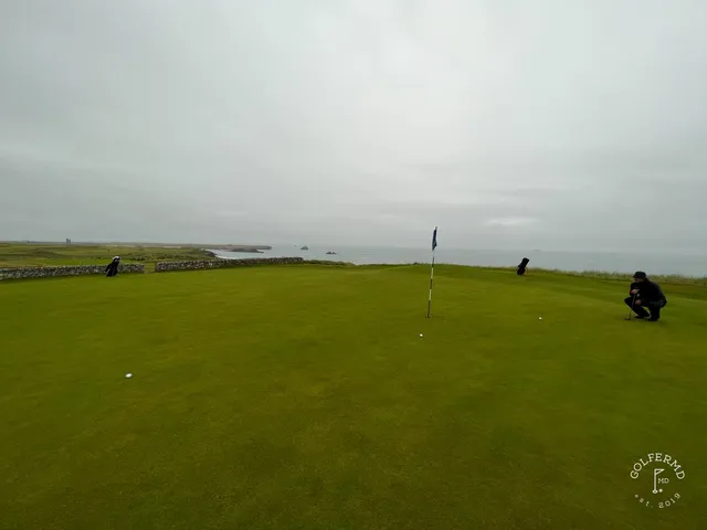 A green at Tralee guarded by sand, with the coastline behind the hole.
