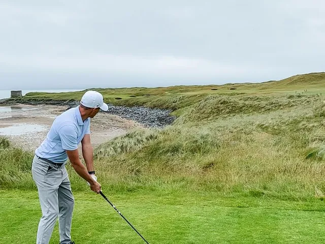 Golfers on a green at Tralee, with the dunes and the Atlantic behind them.