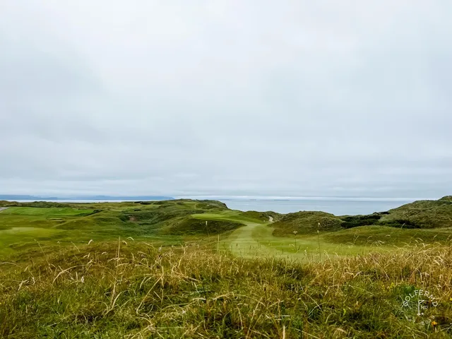 A golfer in the rough at Tralee, with the green and the water ahead.