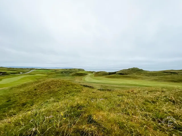 Two bunkers flanking a green at Tralee, with the flagstick and the bay.