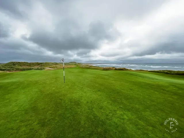 A green at Doonbeg guarded by sand, with the coastline behind the hole.