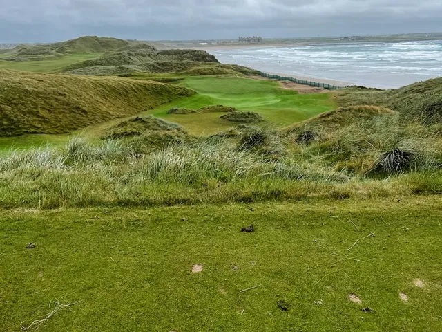 Golfers walking a fairway at Doonbeg, with the ocean beside the hole.