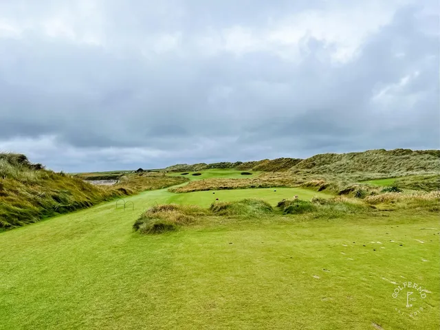 A green at Doonbeg with the flagstick, sand around the hole, and the sea beyond.