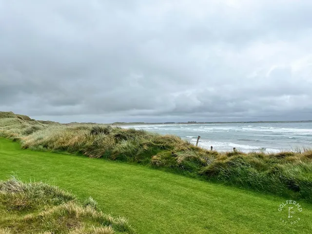 A golfer hitting an approach at Doonbeg, with the bay behind the green.
