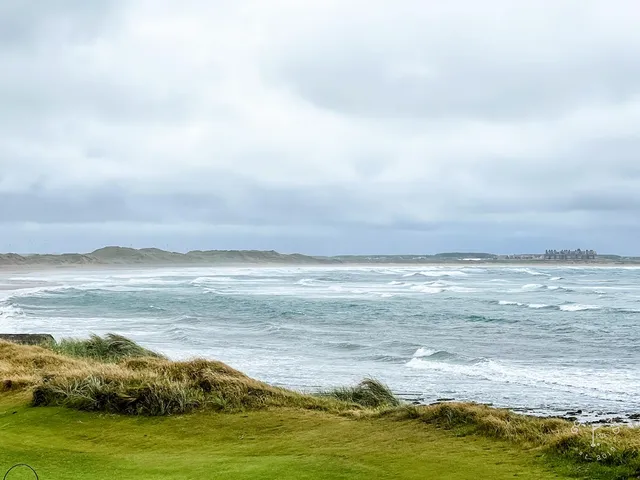 Golfers on a green at Doonbeg, with the dunes and the Atlantic behind them.