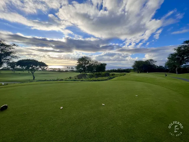 A green and flagstick at the Emerald Course, with the Pacific and mountains behind the hole.