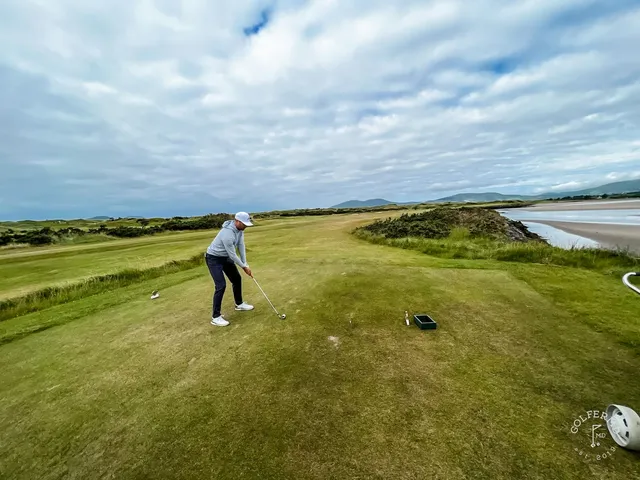 A green and flagstick at Waterville, with a bunker in front and the ocean behind the hole.