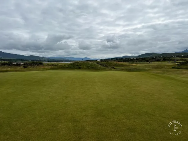 A golfer hitting a shot at Waterville, with the water and the mountains ahead.