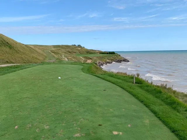 A close view of a flagstick on the Straits Course, with a pot bunker beside the green.