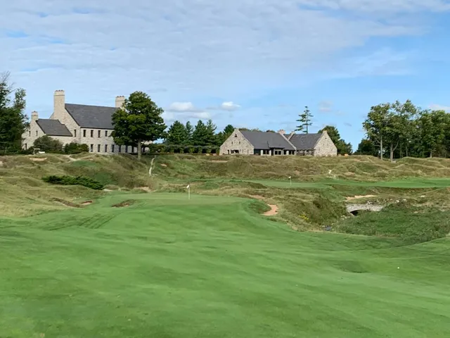 A green and flagstick on the Straits Course seen from the fairway, with the lake on the horizon.