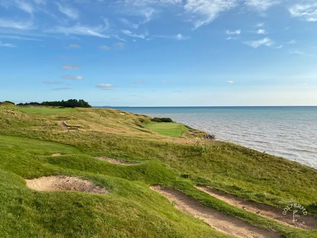 A golfer hitting an approach on the Straits Course, with the lake behind the green.