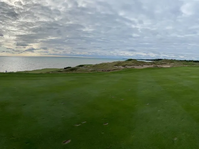A golfer in the rough on the Straits Course, with the green and the water ahead.