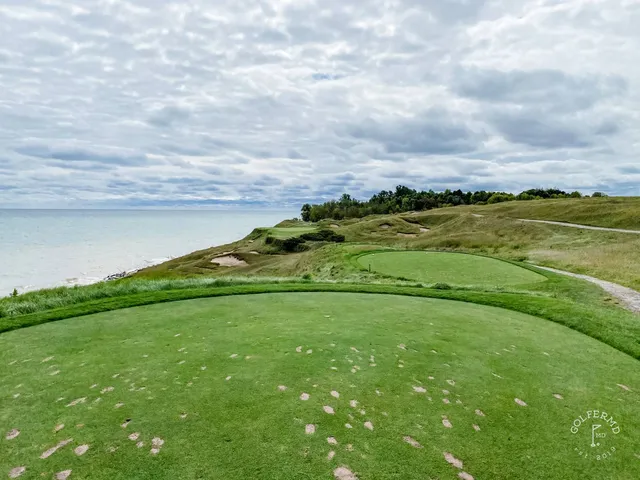 A fairway on the Straits Course pale against the darker dunes, with the lake beyond.