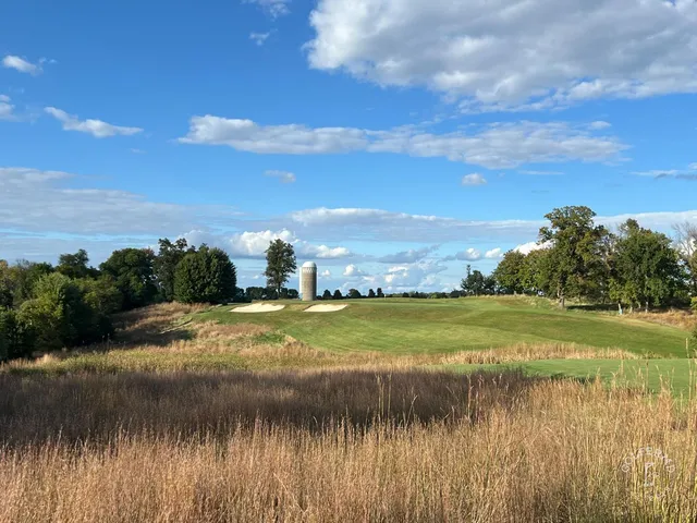 A green and flagstick at Windsong Farm, with a bunker in front and trees behind the hole.