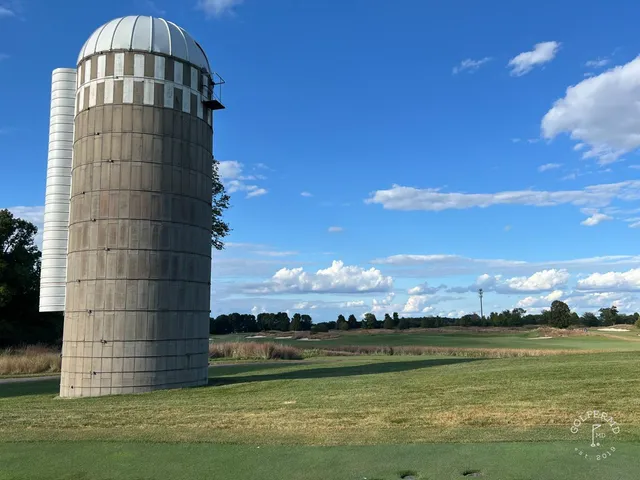 A golfer putting on a green at Windsong Farm, with a bunker and trees beyond the hole.