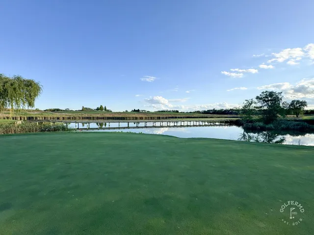 A close view of a flagstick at Windsong Farm, with trees behind the green.