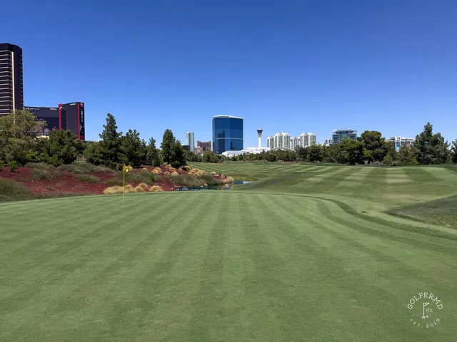 A green and flagstick at Wynn Golf Club, seen from a rise, with the Strip behind the hole.